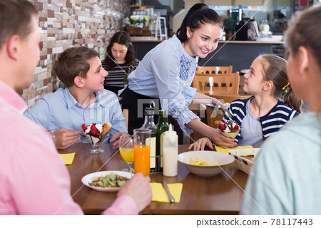 Polite attentive waitress serving dishes to family Polite attentive waitress serving dishes to family 78117443