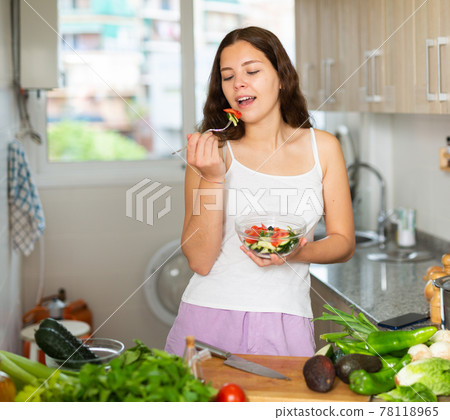 Young woman eating vegetable salad in kitchen Young woman eating vegetable salad in kitchen 78118965