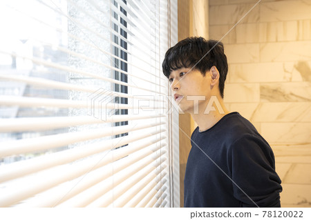 A man looking at the outside scenery through the blinds 78120022