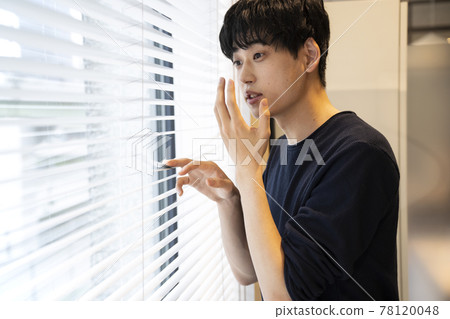 A young man who is surprised to look out from the window blinds A young man who is surprised to look out from the window blinds 78120048