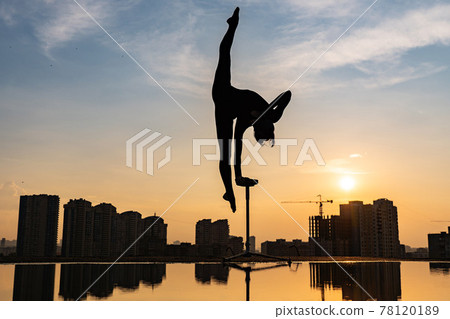 Flexible female circus Artist keep balance on one hand on the rooftop against dramatic sunset and cityscape. Handstand and equilibrium concept  78120189