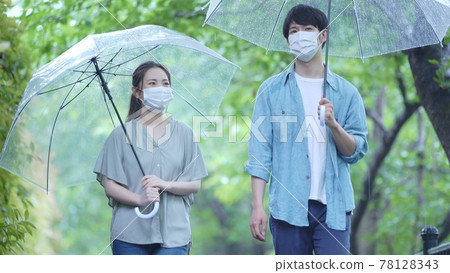 Mask couple walking in the fresh green on a rainy day Mask couple walking in the fresh green on a rainy day 78128343