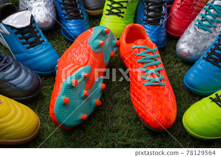 orange soccer shoes lie on the grass surrounded by many colored soccer shoes orange soccer shoes lie on the grass surrounded by many colored soccer shoes 78129564
