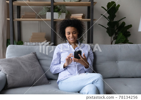 Happy African American woman use smartphone relaxing at home Happy African American woman use smartphone relaxing at home 78134256