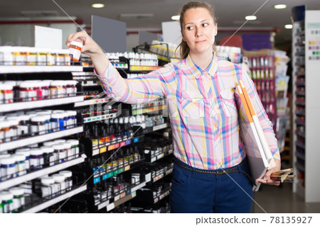 woman customer holding glass jar with color paint in art department 78135927