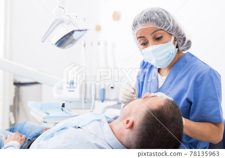 Female dentist in face mask with male patient 78135963