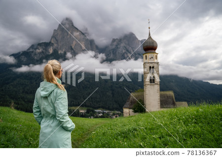 Women enjoy view of St Valentine's Church, Seis am Schlern, Italy. Schlern mountain with rainy clouds in background Women enjoy view of St Valentine's Church, Seis am Schlern, Italy. Schlern mountain with rainy clouds in background 78136367