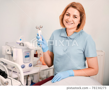 Cheerful female beautician holding facial roller. 78138273