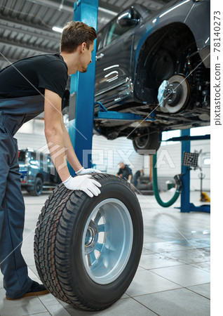 Two male mechanics fixes wheel, car service 78140273