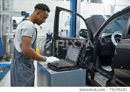 Male mechanic using laptop, car service 78140282