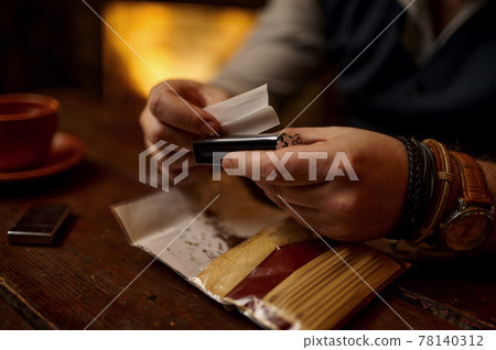 Man grinds tobacco, wooden table on background 78140312