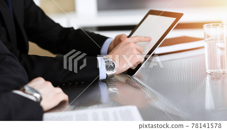 Businessman using tablet computer and work together with his colleague in sunny modern office, close-up. Unknown business people at meeting. Teamwork and partnership concept 78141578