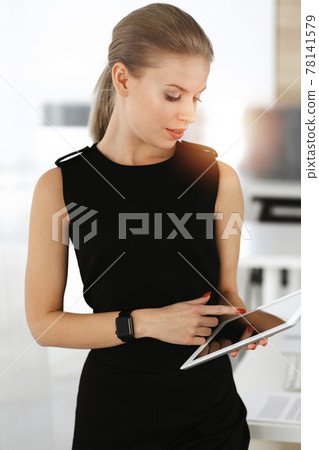 Young blond businesswoman dressed in black dress looks perfect in sunny modern office. Business people concept 78141579