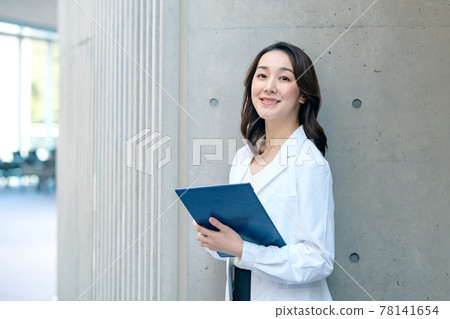Female doctor with a smiling clipboard in a lab coat at the hospital Female doctor with a smiling clipboard in a lab coat at the hospital 78141654