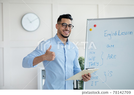Arab male teacher showing thumb up near blackboard, teaching English on web, recommending online foreign language school Arab male teacher showing thumb up near blackboard, teaching English on web, recommending online foreign language school 78142709