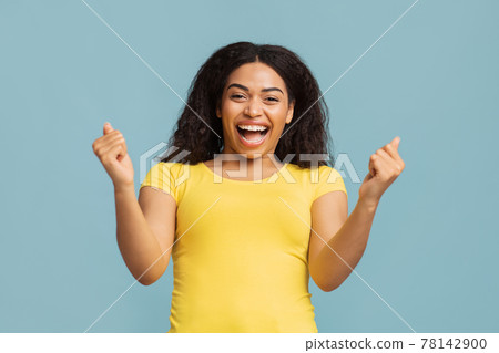Joy of victory. Emotional african american lady cheering and screaming, celebrating victory over blue background Joy of victory. Emotional african american lady cheering and screaming, celebrating victory over blue background 78142900