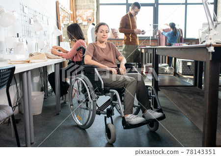 Happy tailor in wheelchair looking at you against colleagues Happy tailor in wheelchair looking at you against colleagues 78143351
