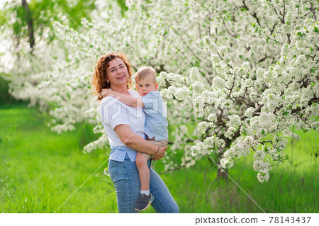 mother holds her young son in a flowering spring garden. parental love and care 78143437