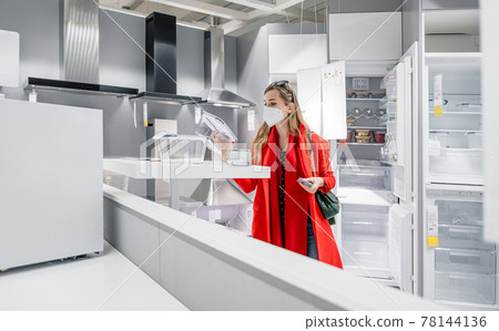 Woman with ffp2 mask shopping white goods in kitchen store 78144136