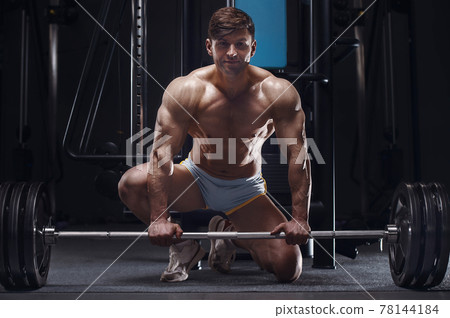 handsome strong athletic man next to a barbell handsome strong athletic man next to a barbell 78144184