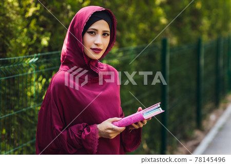 Confident Arab businessman smiling and walks of Dubai. Arab Business vumen hijab is in the streets against the skyscrapers of Dubai. The woman is dressed in a black abaya. Confident Arab businessman smiling and walks of Dubai. Arab Business vumen hijab is in the streets against the skyscrapers of Dubai. The woman is dressed in a black abaya. 78145496