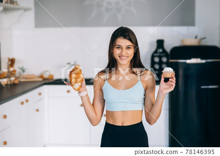 A young woman holds a croissant and a cake in her hands. A young woman holds a croissant and a cake in her hands. 78146395