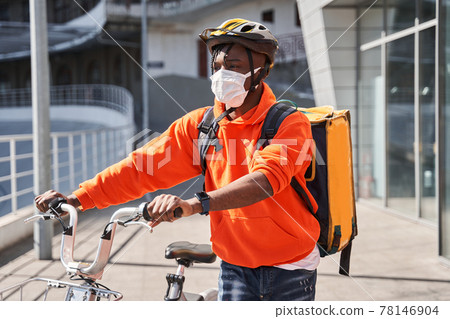 Man wearing helmet with a backpack crossing the road with a bicycle 78146904