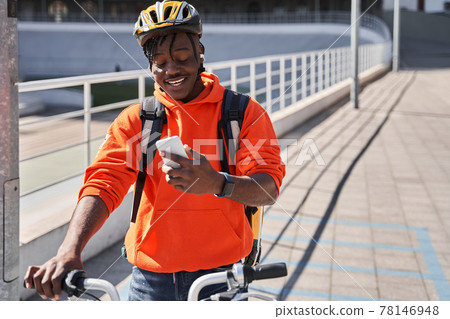 Man wearing helmet and delivery backpack looking at the smartphone screen Man wearing helmet and delivery backpack looking at the smartphone screen 78146948