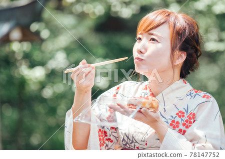 A woman in a yukata eating takoyaki at a summer festival A woman in a yukata eating takoyaki at a summer festival 78147752