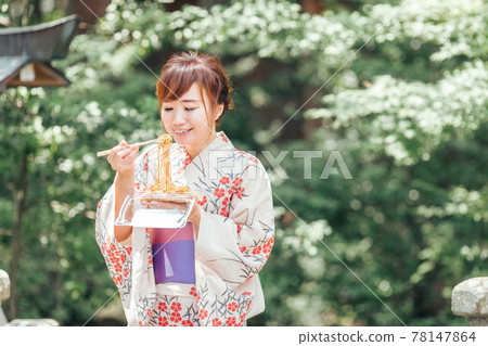 A woman in a yukata eating yakisoba at a summer festival 78147864