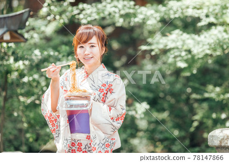 A woman in a yukata eating yakisoba at a summer festival A woman in a yukata eating yakisoba at a summer festival 78147866