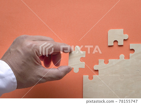 Man's hand inserting piece of puzzle into the jigzaw puzzle on table. 78155747