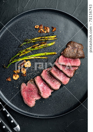 Fillet Mignon tenderloin Grilled and sliced meat beef steaks medium rare, with onion and asparagus, on plate, on black stone background, top view flat lay 78156743
