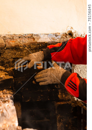 Man destroys an old brick stove, black brick in soot, dismantling the old kitchen surface. Man destroys an old brick stove, black brick in soot, dismantling the old kitchen surface. 78156845