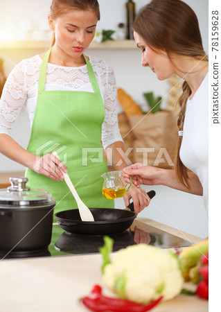 Two women friends choose the recipe and ingredients for a delicious meal in sunny kitchen. Vegetarian concept Two women friends choose the recipe and ingredients for a delicious meal in sunny kitchen. Vegetarian concept 78159628