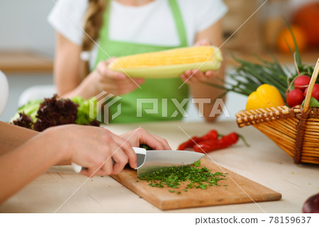Unknown young woman slicing greens for a delicious fresh vegetarian salad while sitting and smiling at the kitchen desk, just hands, close-up. Cooking concept Unknown young woman slicing greens for a delicious fresh vegetarian salad while sitting and smiling at the kitchen desk, just hands, close-up. Cooking concept 78159637