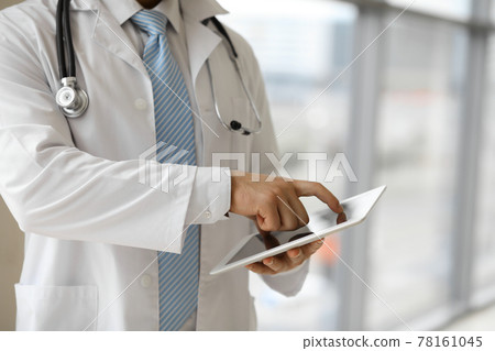 The unknown male doctor is using a tablet computer while standing in a modern clinic, close-up The unknown male doctor is using a tablet computer while standing in a modern clinic, close-up 78161045