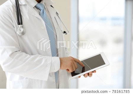 The unknown male doctor is using a tablet computer while standing in a modern clinic, close-up 78161785