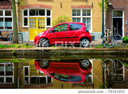 Red car on canal embankment in street of Delft. Delft, Netherlands 78161952