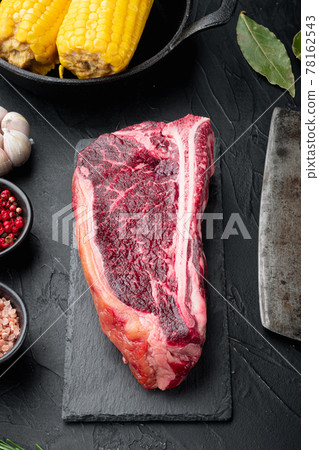 Club raw steak with herbs and salt prepared for cooking, on black stone background Club raw steak with herbs and salt prepared for cooking, on black stone background 78162543