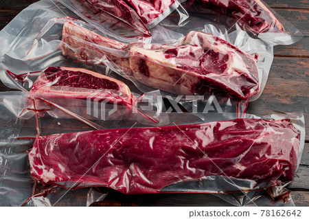 Raw beef meat in the vacuumed skin pack, tomahawk, t bone, club steak, rib eye and tenderloin cuts, on old dark wooden table background 78162642