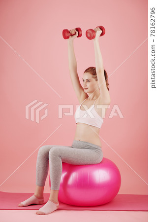 Woman on fitness ball lifting dumbbell Woman on fitness ball lifting dumbbell 78162796