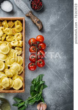 Italian raw handmade Ravioli with fresh ingredients, basil, pesto, ham, mozzarella cheese, parmesan, in wooden box, on gray background, top view flat lay, with copy space for text Italian raw handmade Ravioli with fresh ingredients, basil, pesto, ham, mozzarella cheese, parmesan, in wooden box, on gray background, top view flat lay, with copy space for text 78163419