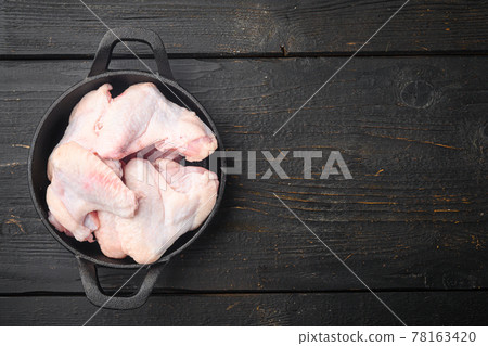 Raw meat. Chicken wings, in frying cast iron pan, on black wooden table background, top view flat lay, with copy space for text Raw meat. Chicken wings, in frying cast iron pan, on black wooden table background, top view flat lay, with copy space for text 78163420