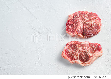 Beef top blade steak, organic meat. White textured background. Top view with space for text. Beef top blade steak, organic meat. White textured background. Top view with space for text. 78163445