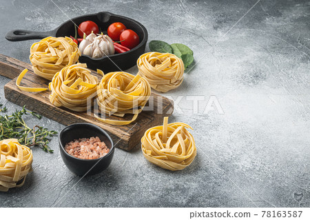 Ingredient of traditional mediterranean cuisine Uncooked pasta tagliatelle, on gray stone background, with copy space for text Ingredient of traditional mediterranean cuisine Uncooked pasta tagliatelle, on gray stone background, with copy space for text 78163587