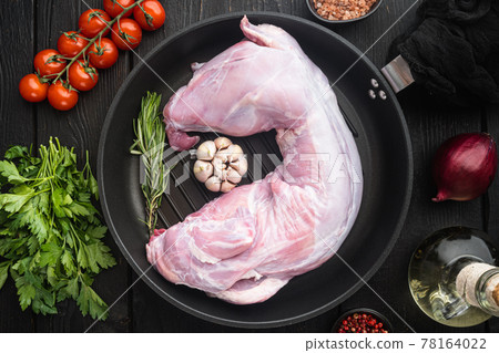 Raw and fresh meat. Whole rabbit ready to cook with ingredients, in cast iron frying pan, on black wooden table background, top view flat lay Raw and fresh meat. Whole rabbit ready to cook with ingredients, in cast iron frying pan, on black wooden table background, top view flat lay 78164022