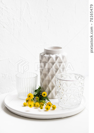 White home decoration with yellow flowers, ceramic vase and glass on tray White home decoration with yellow flowers, ceramic vase and glass on tray 78165479
