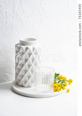 White home decoration with yellow flowers, ceramic vase and glass on tray 78165495