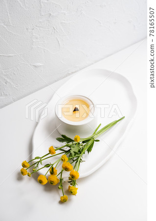 White burning candle with wooden wick and yellow flowers on white tray White burning candle with wooden wick and yellow flowers on white tray 78165507